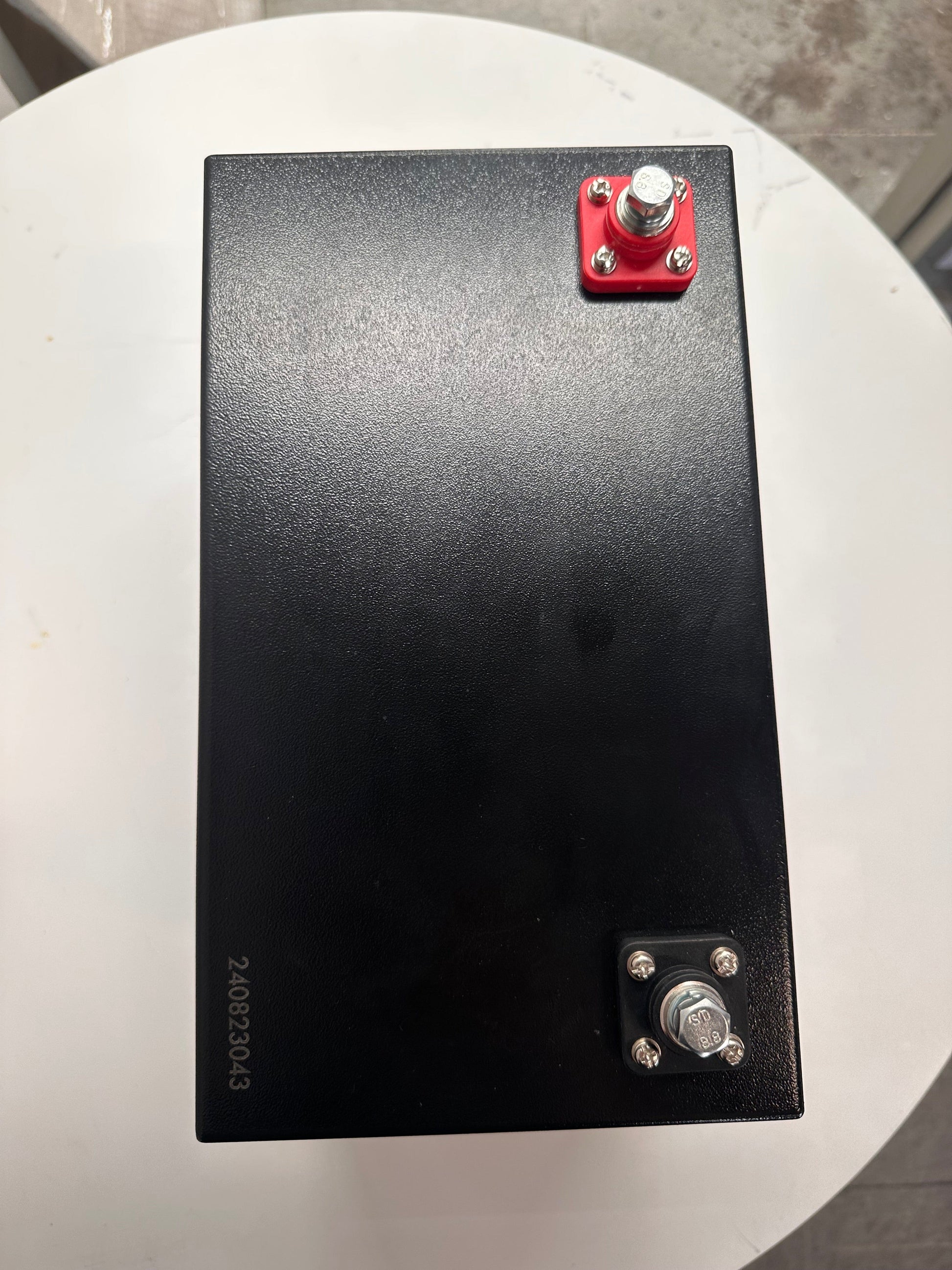 Top view of a 12V lithium battery with metal case, featuring red terminals for connection.